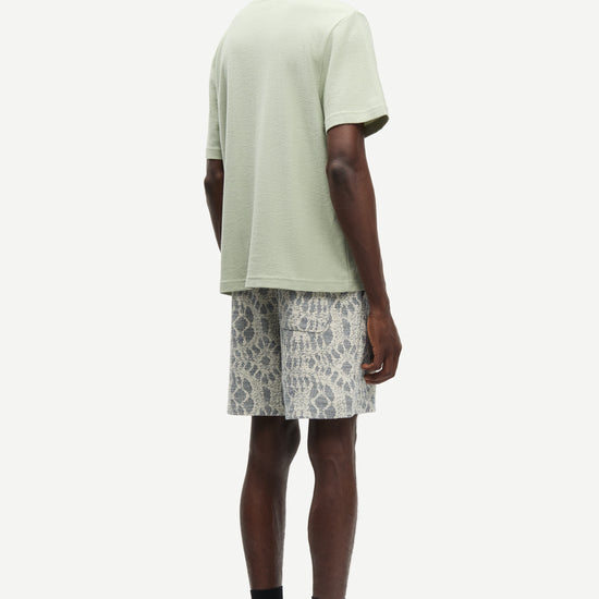 Man wearing a light green t-shirt and patterned shorts on a white background