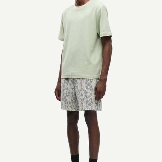Man wearing a light green t-shirt and patterned shorts on a white background