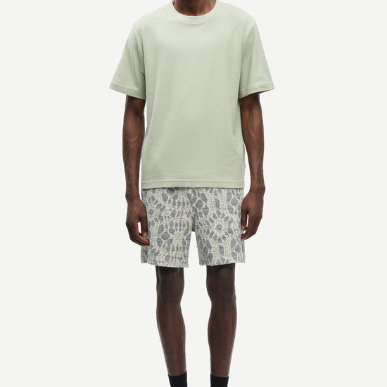 Man wearing a light green t-shirt and patterned shorts on a white background