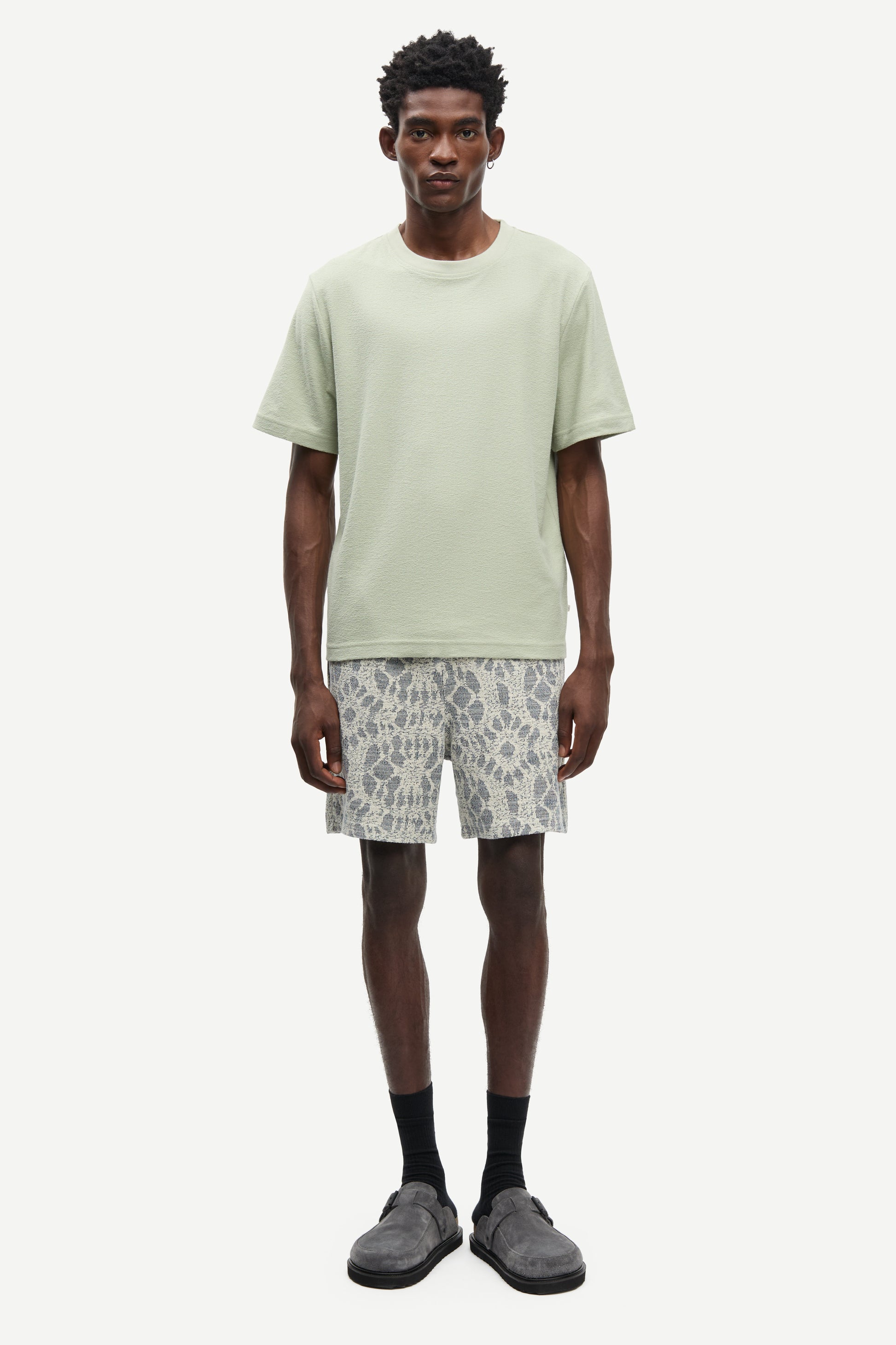 Man wearing a light green t-shirt and patterned shorts on a white background