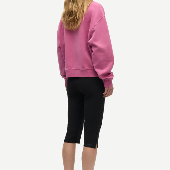 A woman shown from the back wearing a dusty pink crewneck sweatshirt, black capri leggings, and dark gray lace-up shoes against a light gray background.