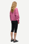 A woman shown from the back wearing a dusty pink crewneck sweatshirt, black capri leggings, and dark gray lace-up shoes against a light gray background.