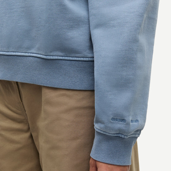 Close-up of a person wearing a light blue sweatshirt and tan pants, showing the ribbed cuffs and hem of the sweatshirt.