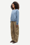 A model wearing a light blue crewneck sweatshirt, wide-leg khaki pants, and brown shoes, standing in profile against a plain light gray background.