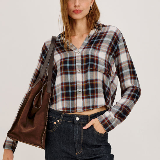 Woman wearing a plaid shirt with a brown leather jacket over her shoulder.