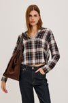 Woman wearing a plaid shirt with a brown leather jacket over her shoulder.