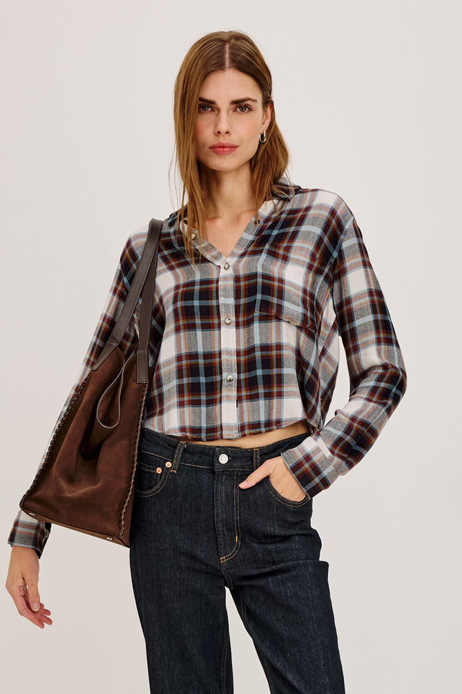 Woman wearing a plaid shirt with a brown leather jacket over her shoulder.