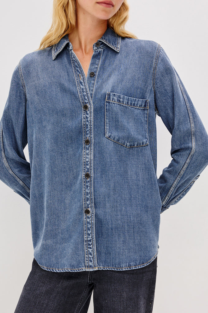 Denim shirt worn by a person on a plain background