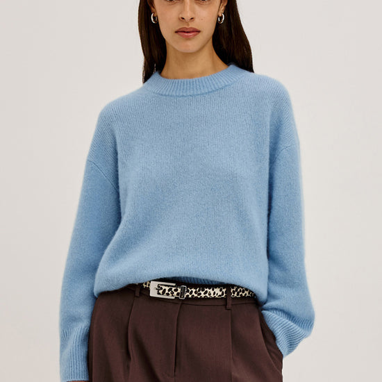 Woman wearing a light blue sweater and brown pants on a plain background