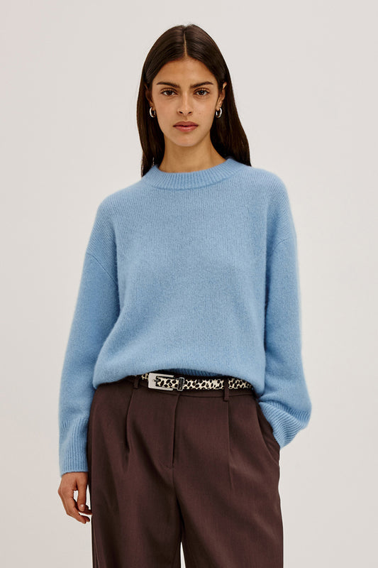 Woman wearing a light blue sweater and brown pants on a plain background