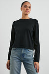 A woman modeling a black long-sleeve crewneck knit top paired with blue jeans, photographed against a light gray studio background.