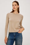 A woman modeling a light beige long-sleeve crewneck sweater paired with blue jeans, photographed against a plain light gray studio background.