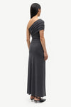 A woman shown from the back wearing a dark charcoal gray one-shoulder maxi dress with a draped neckline and short sleeves, paired with black pointed-toe heels, against a light gray studio background.