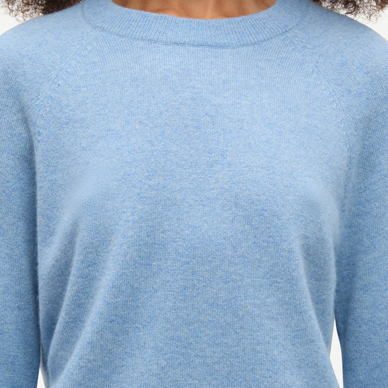 A close-up of a person wearing a light blue crew-neck knit sweater, showing the texture of the fabric and the collar against a plain light background.