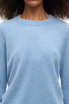 A close-up of a person wearing a light blue crew-neck knit sweater, showing the texture of the fabric and the collar against a plain light background.