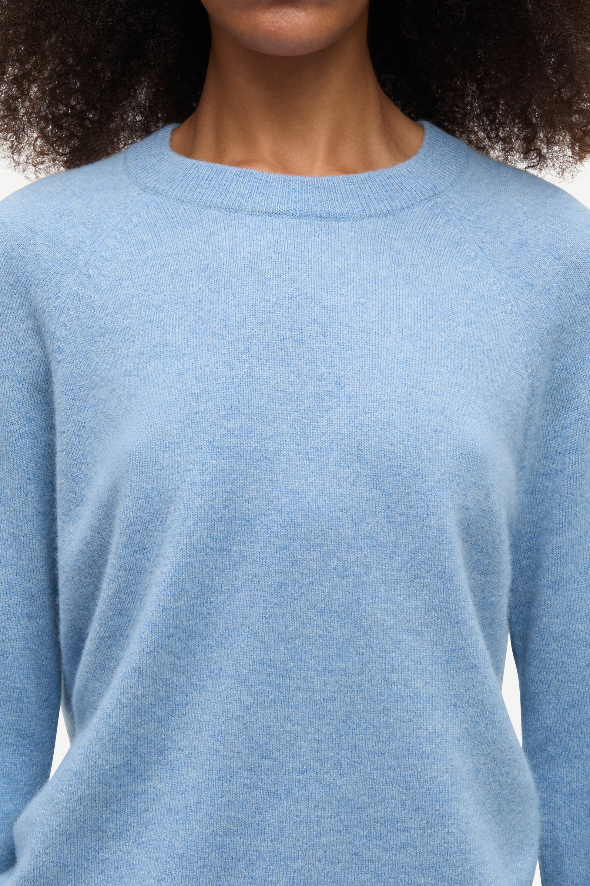 A close-up of a person wearing a light blue crew-neck knit sweater, showing the texture of the fabric and the collar against a plain light background.