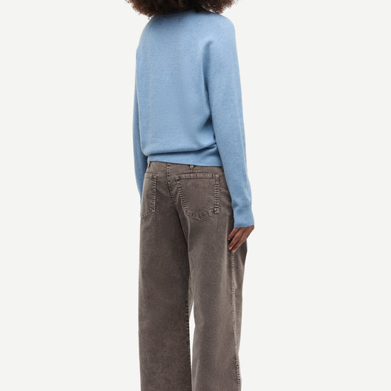 A child model shown from the back wearing a light blue long-sleeve knit top and wide-leg brown corduroy trousers, set against a plain light gray studio background.