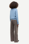 A child model shown from the back wearing a light blue long-sleeve knit top and wide-leg brown corduroy trousers, set against a plain light gray studio background.