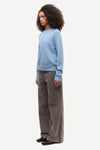 A model wearing a light blue crewneck sweater and wide-leg brown corduroy trousers, standing in profile against a plain light gray background.