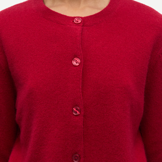 A close-up of a person wearing a bright red knit cardigan sweater with matching red buttons, shown against a plain light background.