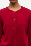 A close-up of a person wearing a bright red knit cardigan sweater with matching red buttons, shown against a plain light background.