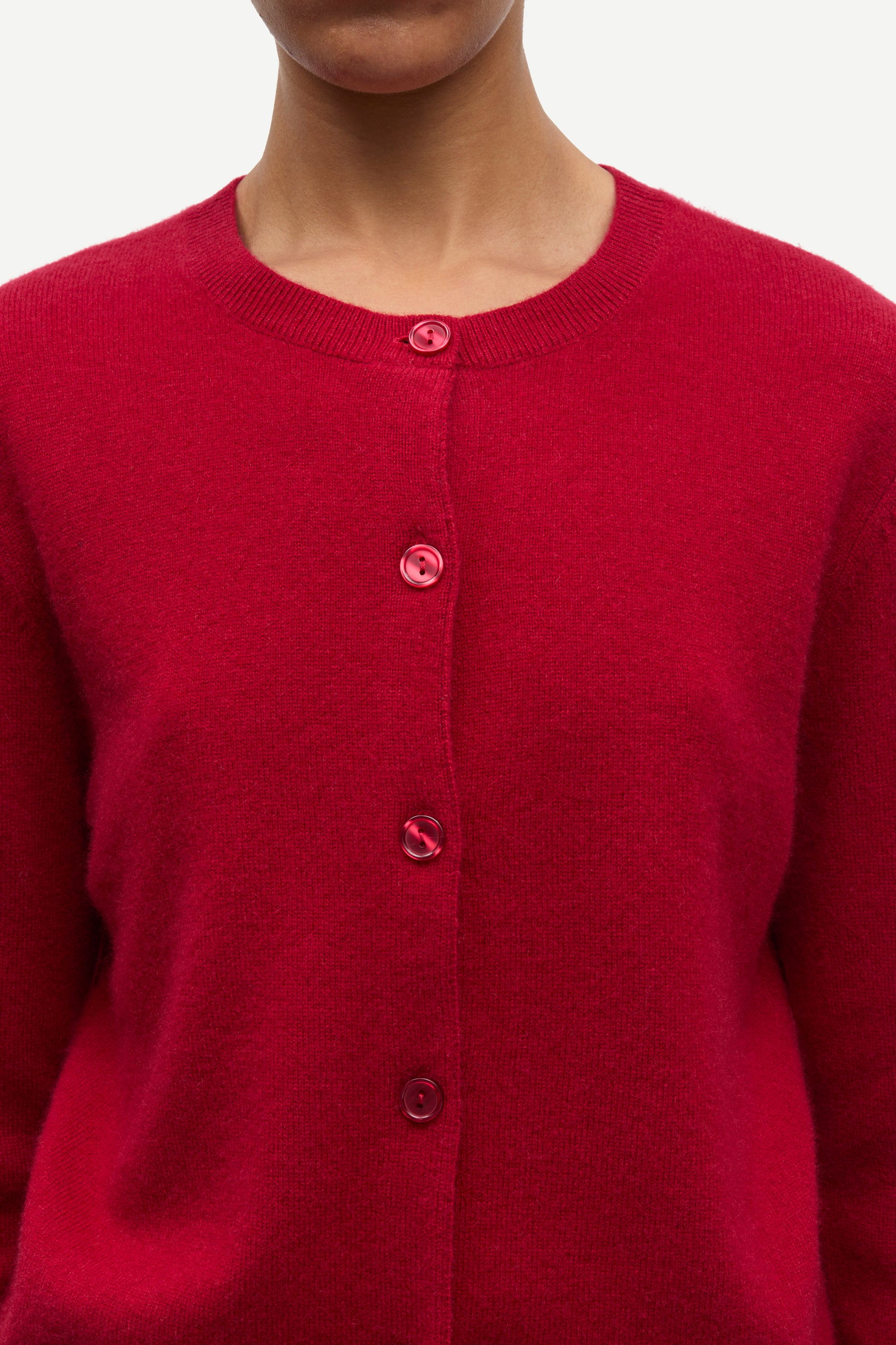 A close-up of a person wearing a bright red knit cardigan sweater with matching red buttons, shown against a plain light background.