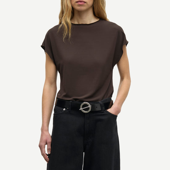 A woman modeling a dark brown short-sleeve top and black wide-leg trousers with a black belt, photographed against a light gray studio background.