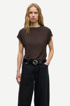 A woman modeling a dark brown short-sleeve top and black wide-leg trousers with a black belt, photographed against a light gray studio background.