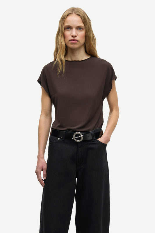 A woman modeling a dark brown short-sleeve top and black wide-leg trousers with a black belt, photographed against a light gray studio background.