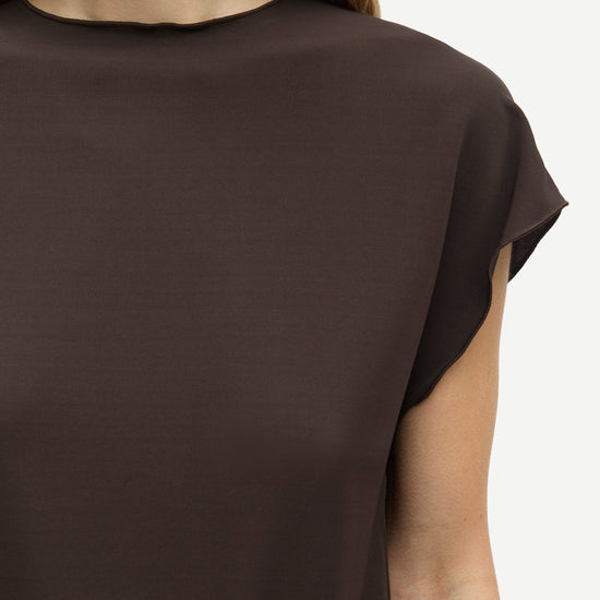 Close-up of a model wearing a dark brown short-sleeve top against a light gray background.