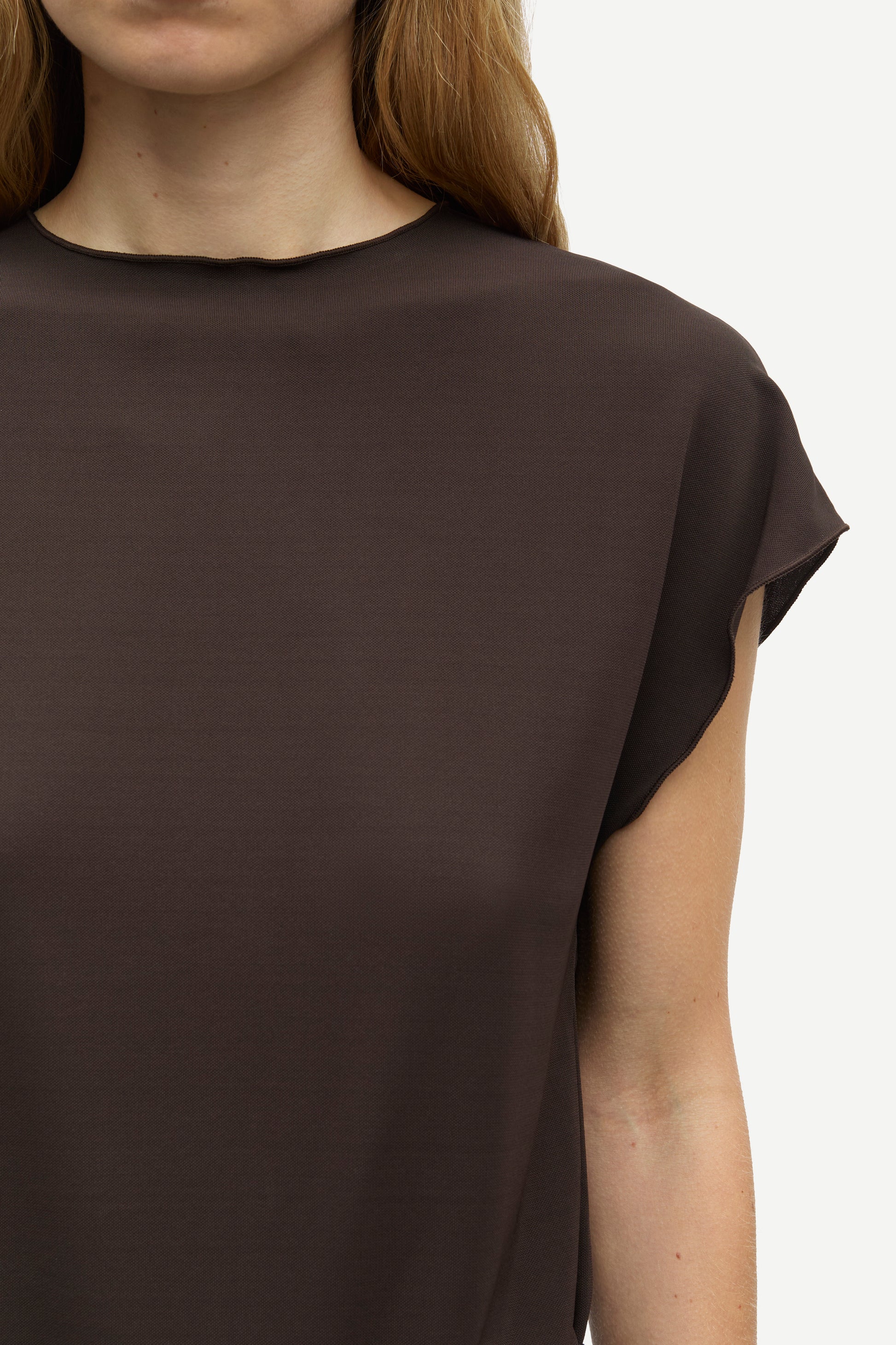 Close-up of a model wearing a dark brown short-sleeve top against a light gray background.
