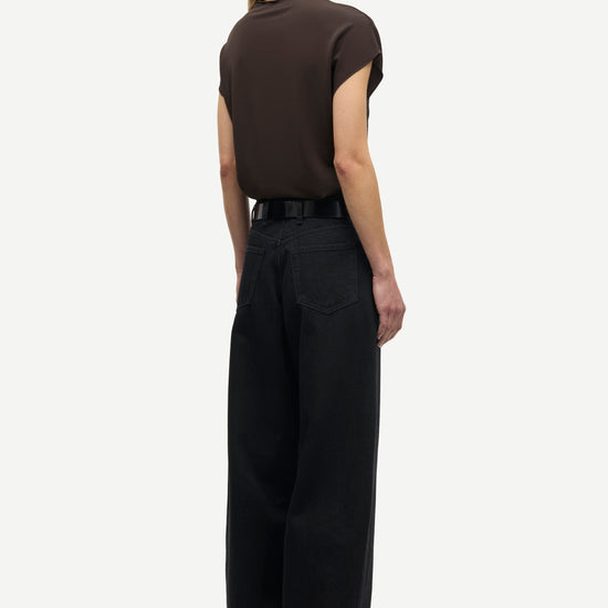 A model shown from the back wearing a dark brown short-sleeve top and black wide-leg trousers, standing against a light gray background.