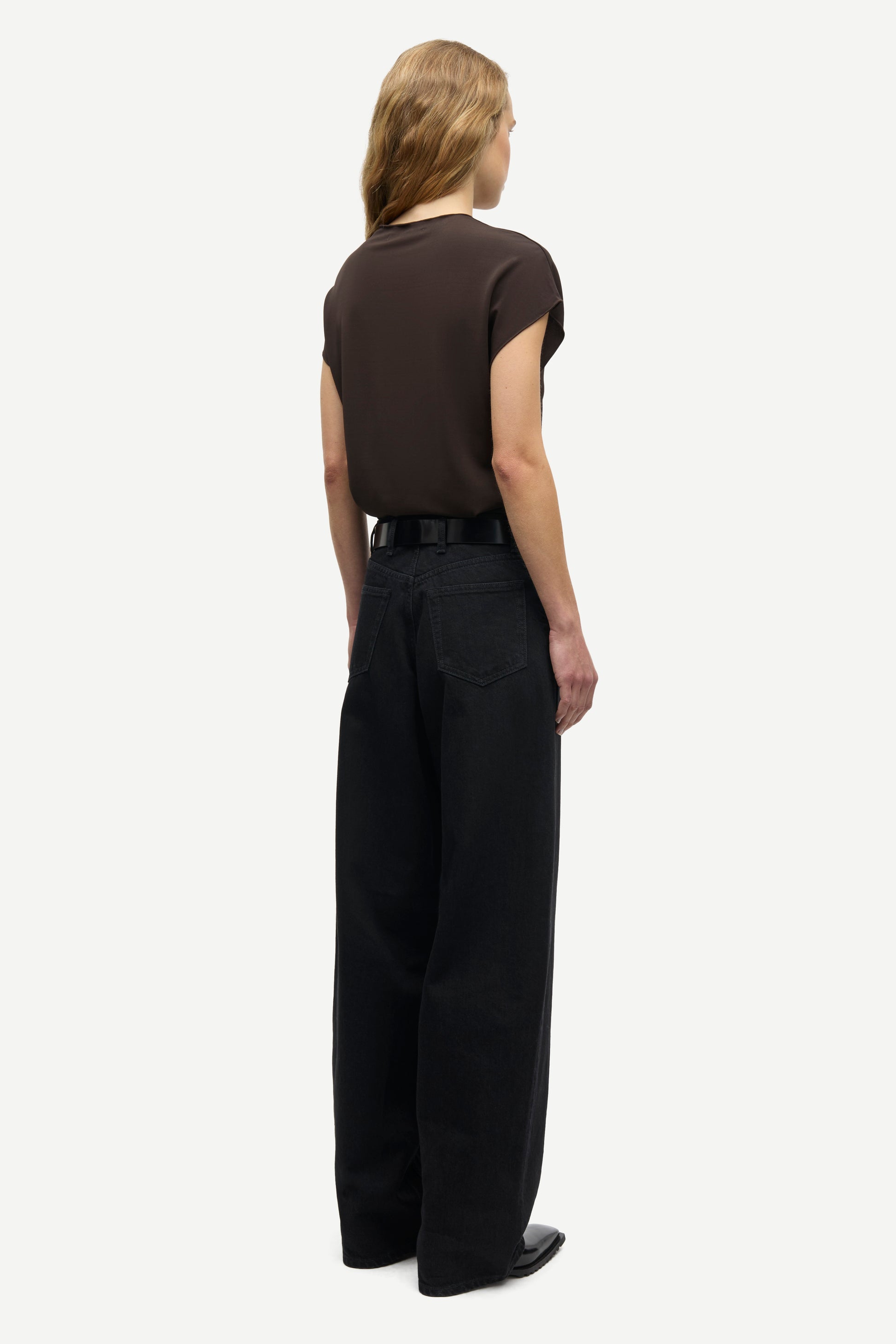 A model shown from the back wearing a dark brown short-sleeve top and black wide-leg trousers, standing against a light gray background.
