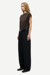 A model stands in profile wearing a dark brown short-sleeve top, black wide-leg trousers, and a black belt with a silver buckle, against a plain light gray studio background.
