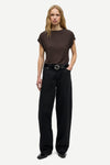 A woman modeling a dark brown short-sleeve crewneck t-shirt and black wide-leg trousers with a black belt, standing against a light gray studio background.