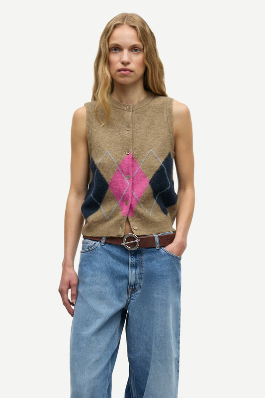 A woman modeling a sleeveless button-front knit vest with an argyle pattern in beige, dark navy, and bright pink, paired with blue jeans and a brown belt against a light gray studio background.