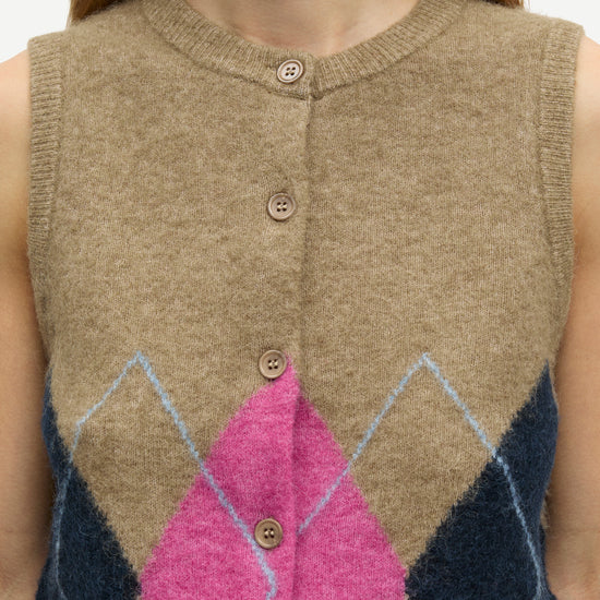 A close-up of a person wearing a sleeveless knit button-front vest in beige with a large pink diamond and navy blue argyle-style geometric pattern on the lower front.