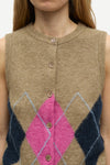 A close-up of a person wearing a sleeveless knit button-front vest in beige with a large pink diamond and navy blue argyle-style geometric pattern on the lower front.