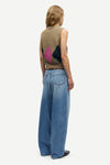 A model shown from the back wearing a brown sleeveless knit vest with a pink and black geometric pattern on the back, paired with wide-leg blue jeans, against a light gray background.