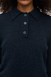 Close-up of a person wearing a dark navy knit polo sweater with a three-button placket.