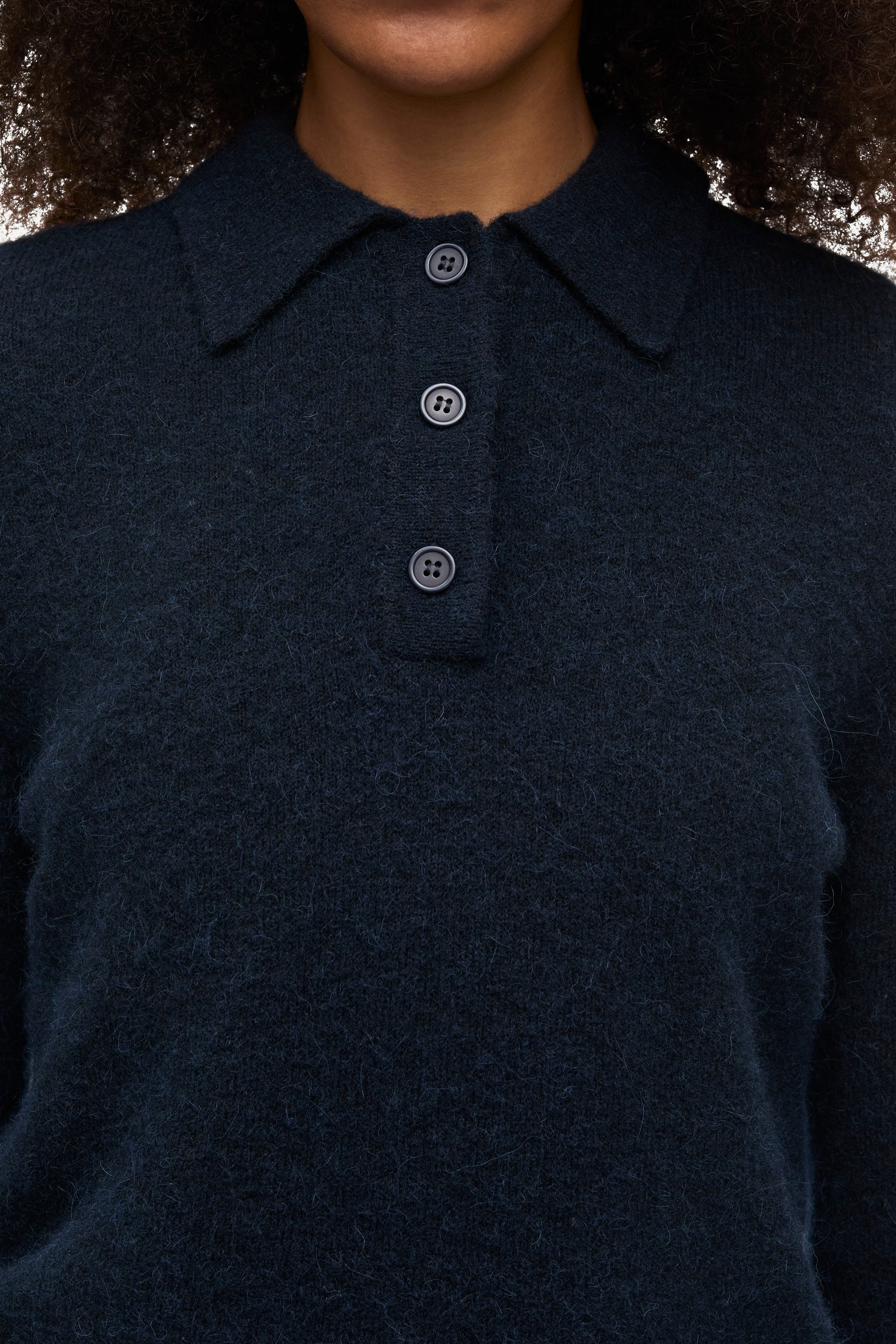 Close-up of a person wearing a dark navy knit polo sweater with a three-button placket.