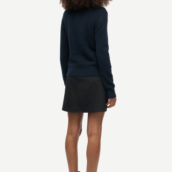 A model shown from the back wearing a dark navy blue long-sleeve knit sweater, a black mini skirt, and black ankle boots, set against a plain light gray background.