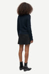 A model shown from the back wearing a dark navy blue long-sleeve knit sweater, a black mini skirt, and black ankle boots, set against a plain light gray background.