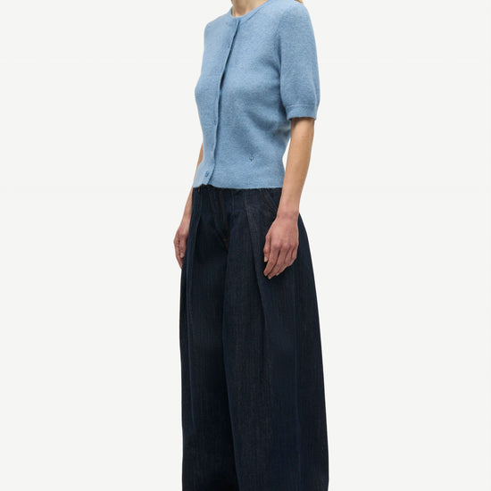 A woman modeling a light blue short-sleeve knit top and dark navy wide-leg trousers against a plain light gray studio background.
