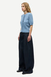 A woman modeling a light blue short-sleeve knit top and dark navy wide-leg trousers against a plain light gray studio background.