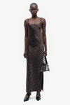 A model wearing a dark brown sheer mesh slip dress with a black polka dot pattern, holding a small black handbag against a light gray background.