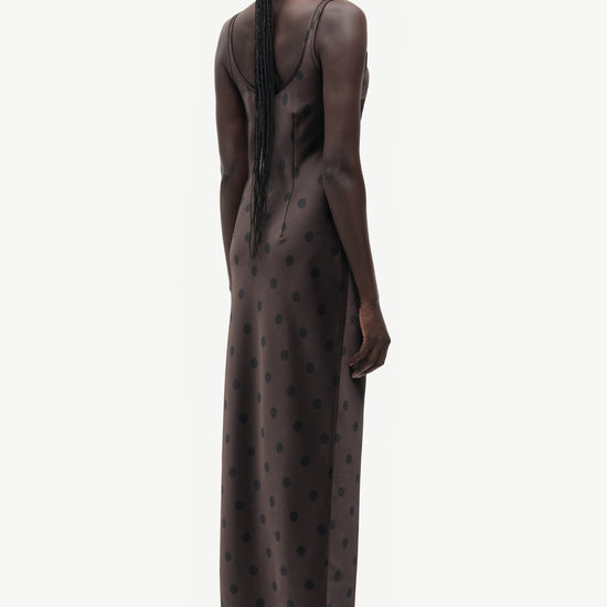 A model shown from the back wearing a dark brown sleeveless maxi dress with a subtle polka dot pattern, paired with black pointed-toe heels, against a plain light gray background.