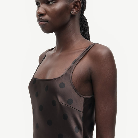 A model shown in profile wearing a dark brown camisole top with black polka dots, set against a plain light gray background.