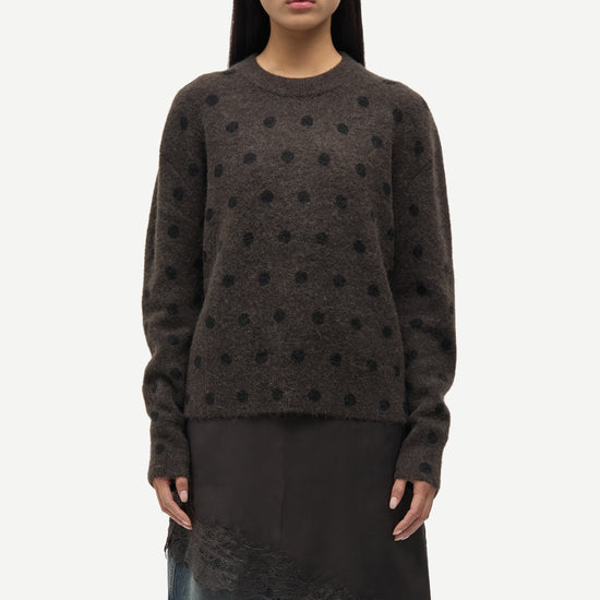 Person wearing a dark brown sweater with black polka dots on a white background