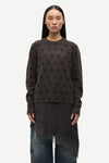 Person wearing a dark brown sweater with black polka dots on a white background